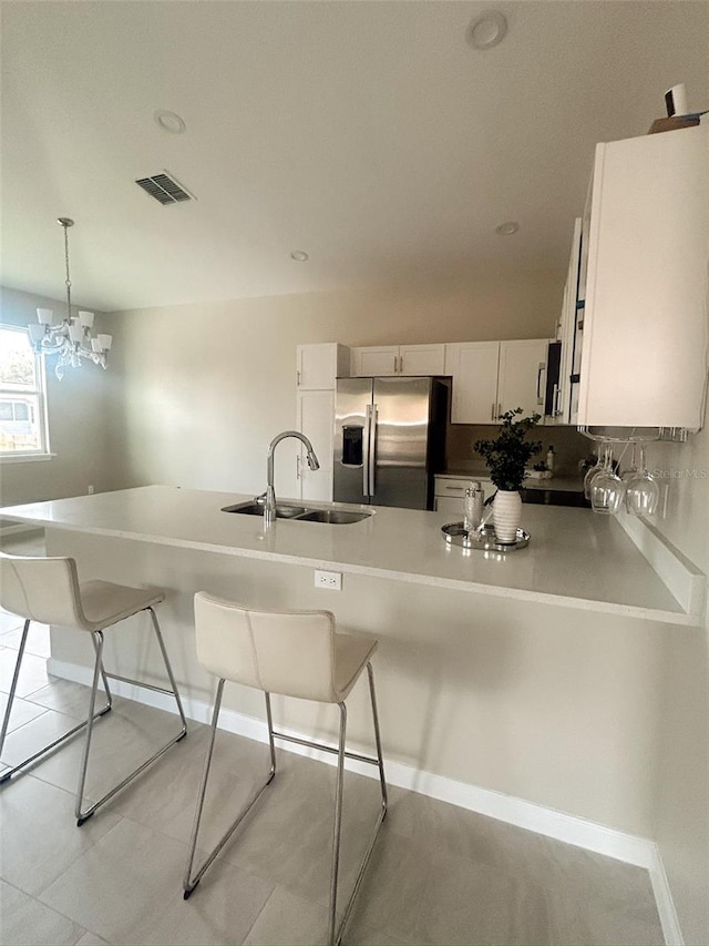 kitchen with visible vents, a sink, stainless steel fridge, a peninsula, and a kitchen bar