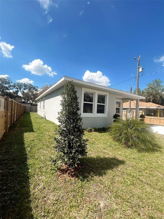 view of side of home featuring a fenced backyard, a yard, and stucco siding