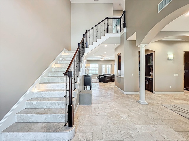 stairs featuring ceiling fan, a high ceiling, and decorative columns