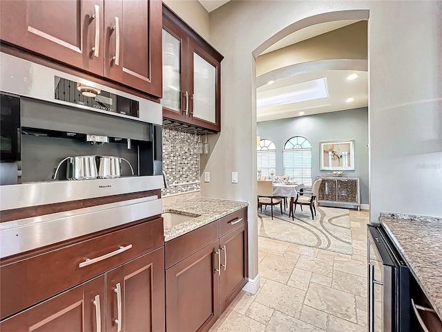 kitchen with oven, decorative backsplash, light stone countertops, a tray ceiling, and beverage cooler