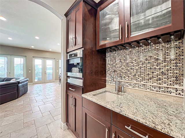 kitchen with french doors, tasteful backsplash, light stone counters, and sink