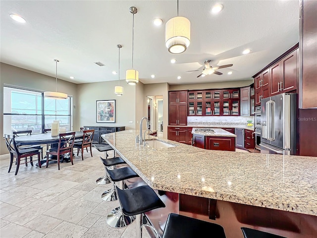 kitchen featuring ceiling fan, sink, hanging light fixtures, high end refrigerator, and an island with sink