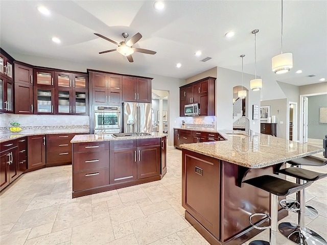 kitchen with backsplash, hanging light fixtures, sink, an island with sink, and appliances with stainless steel finishes