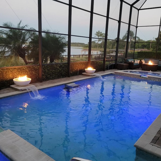 pool at dusk featuring pool water feature, a water view, a fire pit, and a lanai