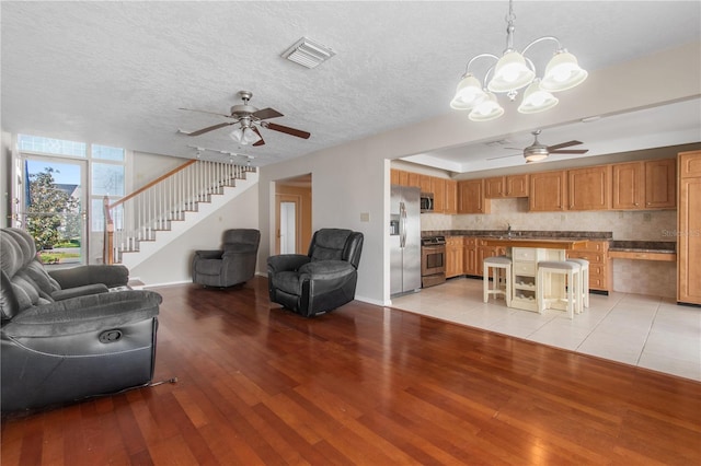 living room with sink, ceiling fan with notable chandelier, light hardwood / wood-style floors, and a textured ceiling