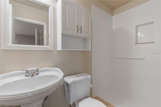 bathroom featuring tiled shower, sink, and toilet