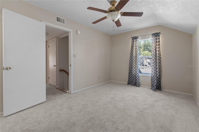 empty room with a textured ceiling, light colored carpet, vaulted ceiling, and ceiling fan