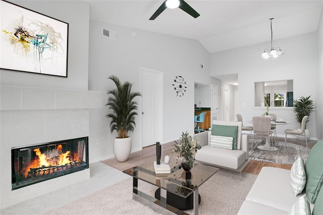 living room featuring a tiled fireplace, light hardwood / wood-style flooring, ceiling fan with notable chandelier, and vaulted ceiling