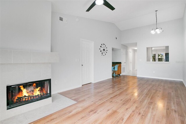 unfurnished living room featuring high vaulted ceiling, ceiling fan with notable chandelier, light wood-type flooring, and a tile fireplace