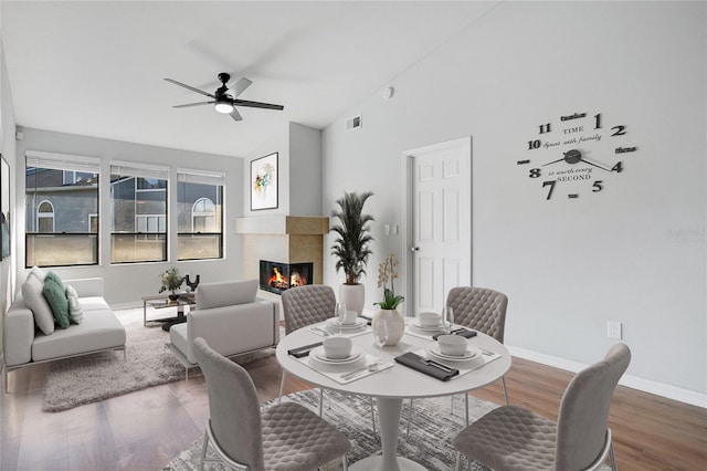 dining room with a tiled fireplace, ceiling fan, hardwood / wood-style floors, and vaulted ceiling