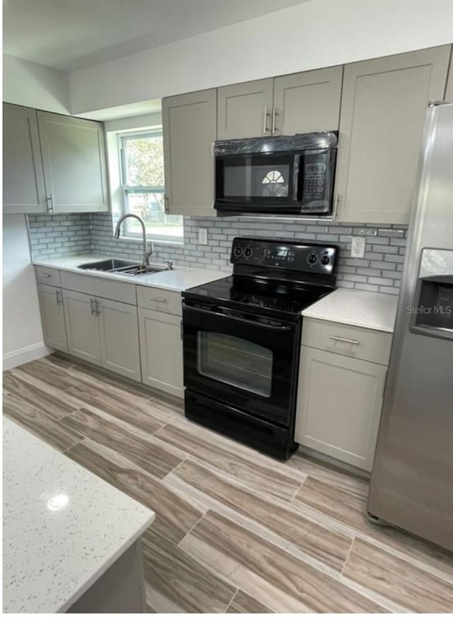 kitchen with sink, light hardwood / wood-style flooring, backsplash, gray cabinets, and black appliances