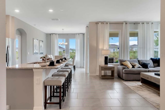 interior space with pendant lighting, a breakfast bar, sink, a notable chandelier, and stainless steel refrigerator