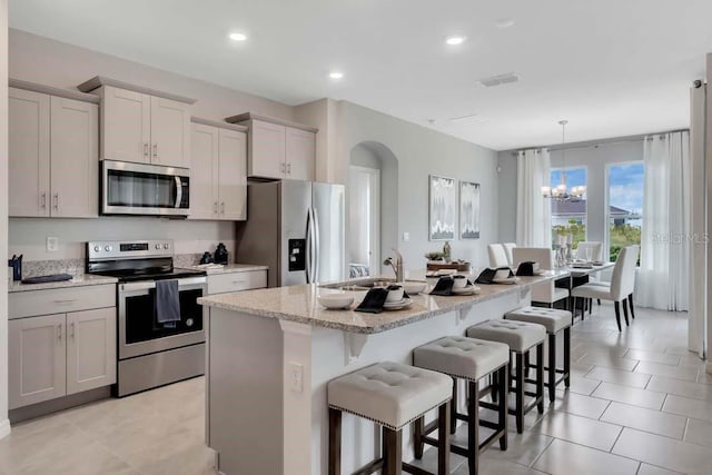 kitchen with a kitchen island with sink, light stone countertops, decorative light fixtures, a kitchen bar, and stainless steel appliances