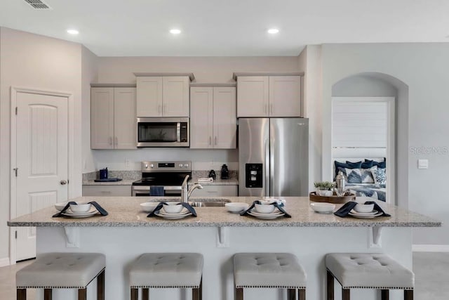 kitchen featuring a breakfast bar area, a kitchen island with sink, light stone countertops, and appliances with stainless steel finishes