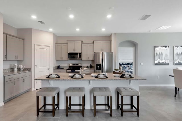 kitchen featuring a breakfast bar, appliances with stainless steel finishes, gray cabinets, and an island with sink