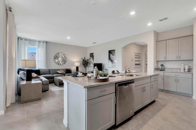 kitchen with stainless steel dishwasher, light stone counters, sink, and a kitchen island with sink