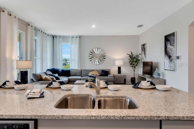 kitchen featuring dishwashing machine, light stone counters, and sink