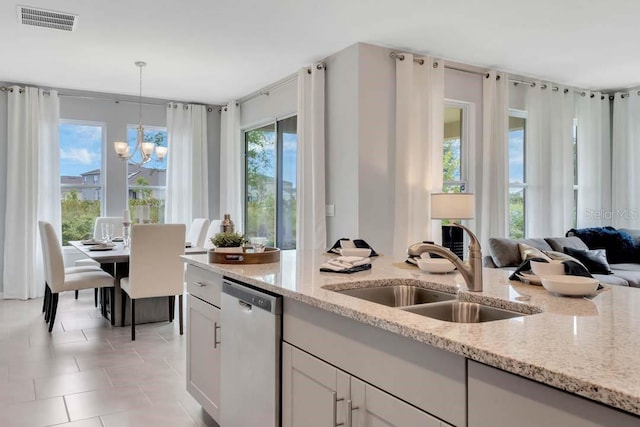 kitchen featuring light stone countertops, sink, pendant lighting, a notable chandelier, and dishwasher