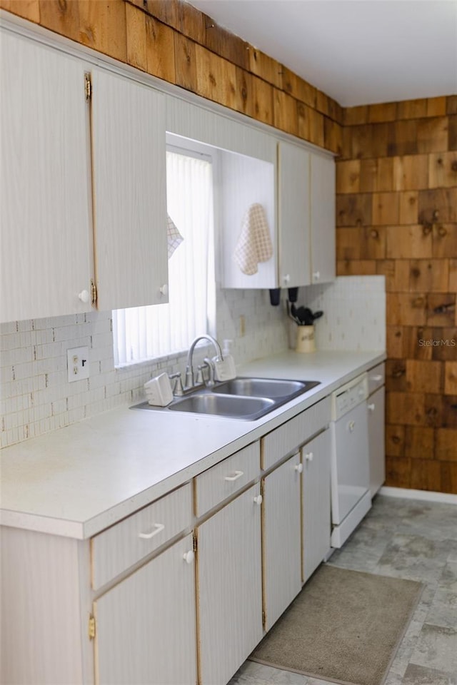 kitchen featuring backsplash, dishwasher, wood walls, and sink