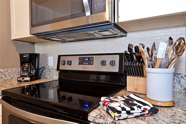 interior details featuring decorative backsplash, electric range, white cabinets, and light stone countertops