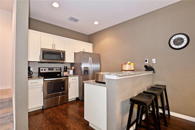 kitchen featuring a breakfast bar area, white cabinetry, dark hardwood / wood-style flooring, kitchen peninsula, and stainless steel appliances