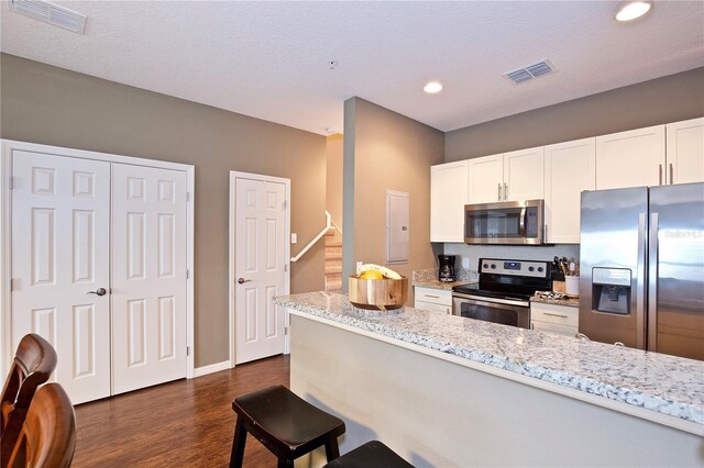 kitchen with white cabinets, appliances with stainless steel finishes, dark hardwood / wood-style floors, and light stone counters