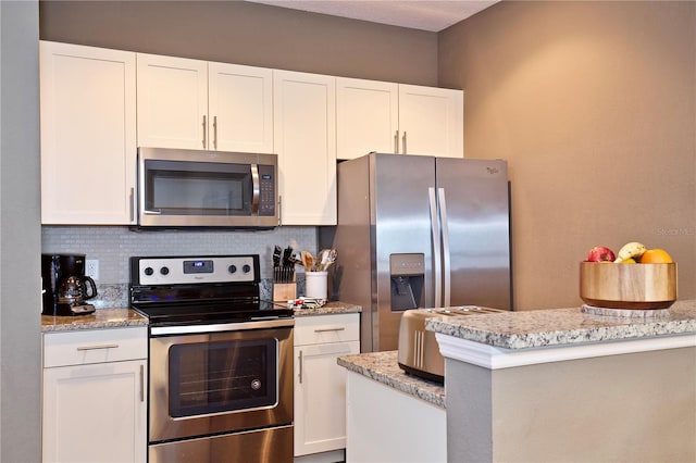 kitchen featuring stainless steel appliances, white cabinetry, tasteful backsplash, and light stone counters