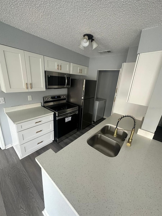 kitchen featuring appliances with stainless steel finishes, a textured ceiling, dark wood-type flooring, sink, and white cabinets