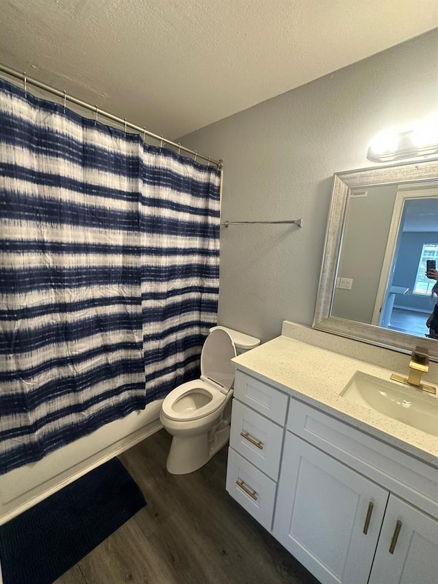 full bathroom with vanity, hardwood / wood-style flooring, toilet, shower / bath combo with shower curtain, and a textured ceiling