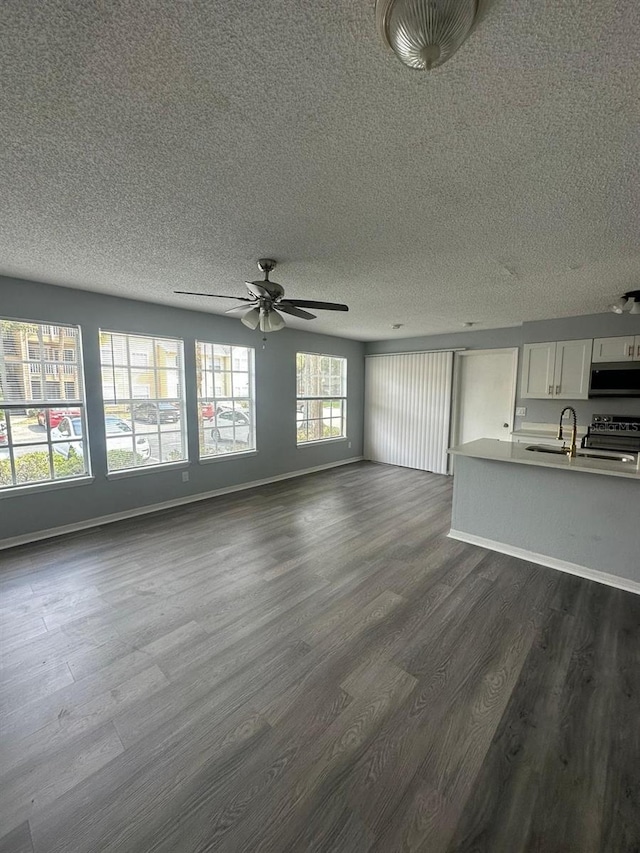 unfurnished living room with ceiling fan, sink, dark wood-type flooring, and a textured ceiling