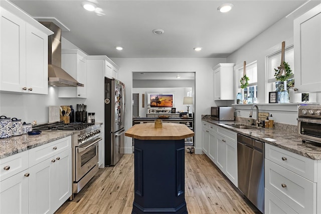 kitchen with wood counters, stainless steel appliances, sink, wall chimney range hood, and a center island