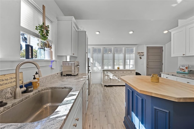 kitchen featuring sink, a kitchen island, butcher block countertops, light hardwood / wood-style floors, and white cabinetry