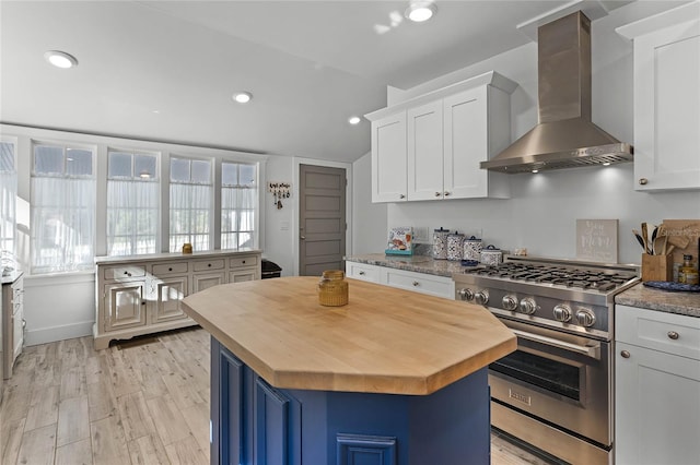 kitchen with white cabinets, wall chimney range hood, high end stainless steel range, a kitchen island, and butcher block counters