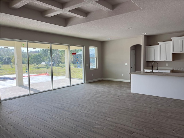 unfurnished living room with a textured ceiling, sink, beamed ceiling, and coffered ceiling