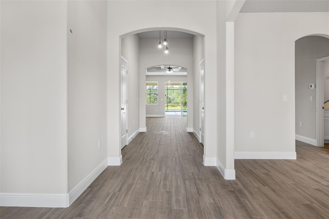 foyer featuring a ceiling fan, baseboards, arched walkways, and dark wood-style flooring