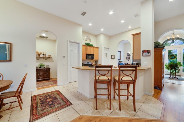 kitchen featuring kitchen peninsula, a kitchen bar, light wood-type flooring, an inviting chandelier, and stainless steel stove