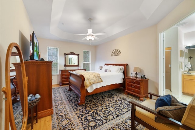 bedroom featuring connected bathroom, a tray ceiling, ceiling fan, and light hardwood / wood-style floors