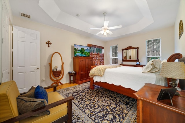 bedroom with wood-type flooring, a raised ceiling, and ceiling fan