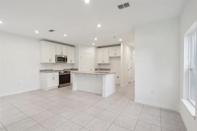 kitchen with light stone countertops, a center island with sink, white cabinetry, and stainless steel appliances