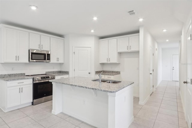 kitchen with light stone countertops, stainless steel appliances, a kitchen island with sink, sink, and white cabinetry