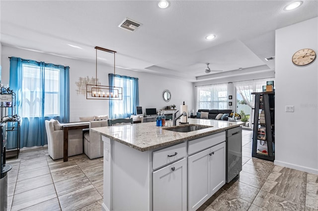 kitchen with sink, ceiling fan, an island with sink, light stone counters, and white cabinetry