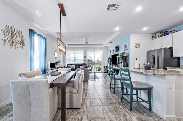 kitchen with hanging light fixtures, ceiling fan, stainless steel fridge, light stone counters, and white cabinetry