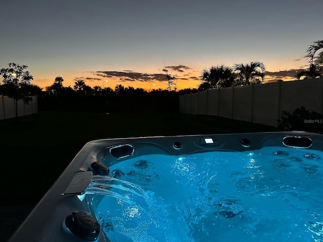 pool at dusk featuring a hot tub