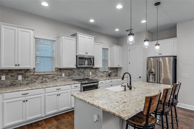 kitchen with stainless steel appliances, sink, decorative light fixtures, a center island with sink, and white cabinetry