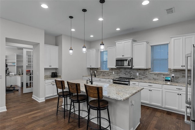 kitchen with hanging light fixtures, white cabinetry, a kitchen island with sink, and appliances with stainless steel finishes