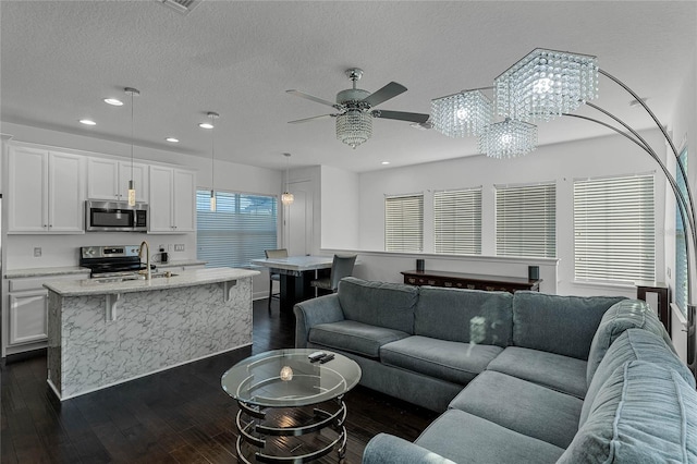 living room featuring sink, ceiling fan with notable chandelier, dark wood-type flooring, and a textured ceiling