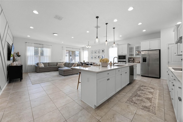 kitchen with a kitchen island with sink, sink, black appliances, white cabinetry, and hanging light fixtures