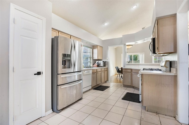 kitchen with light brown cabinets, stainless steel appliances, light tile patterned floors, and a wealth of natural light