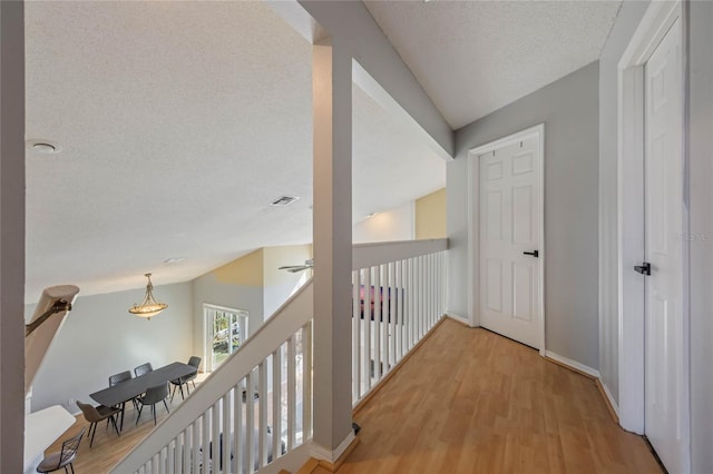 hall with a textured ceiling, light hardwood / wood-style flooring, and lofted ceiling