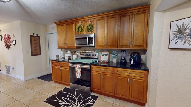 kitchen with light tile patterned floors, visible vents, appliances with stainless steel finishes, brown cabinets, and a textured ceiling